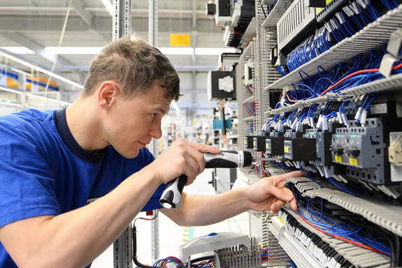 Ein junger Mann arbeitet an einem Schaltkasten in einer Industriehalle
