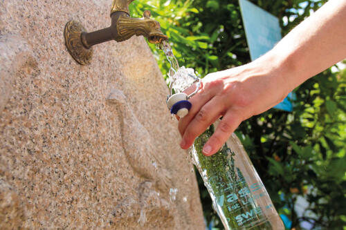 Ein Trinkwasserbrunnen an dem jemand eine Flasche auffüllt Ein Trinkwasserbrunnen an dem jemand eine Flasche auffüllt